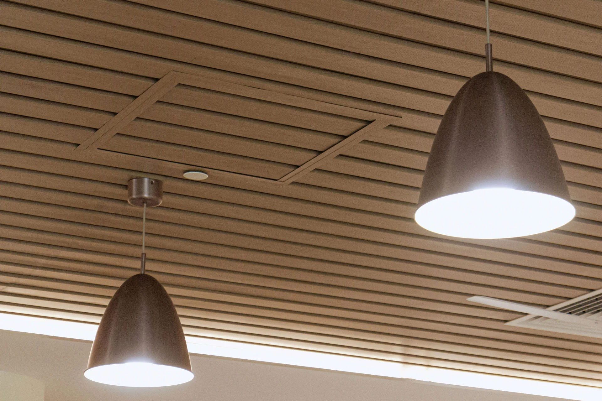 Two modern pendant lights with cone-shaped shades hang from a ceiling made of parallel wooden slats. The lights are switched on, illuminating the area below.
