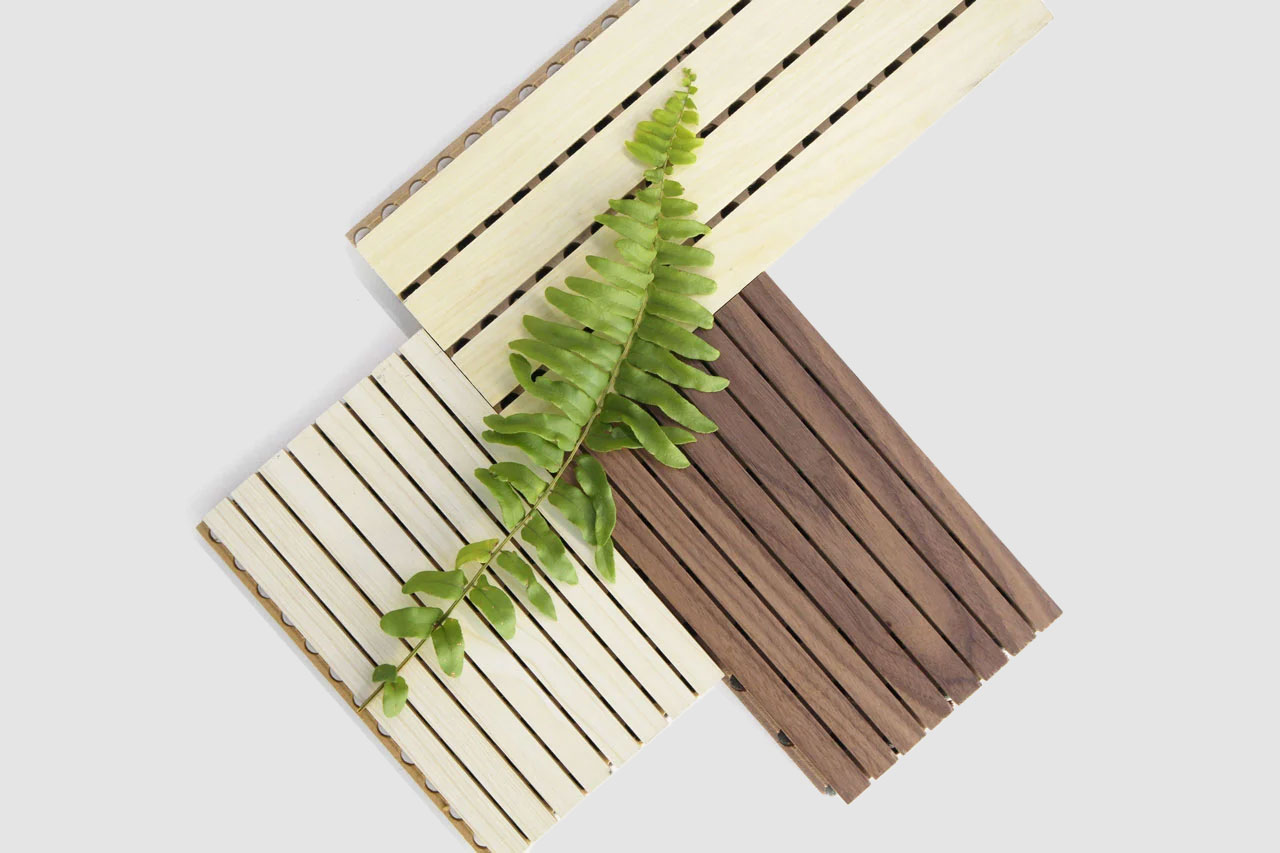 Three rectangular wooden slat panels—two light-colored and one dark—overlap on a white background. A green fern leaf is placed diagonally across the panels.