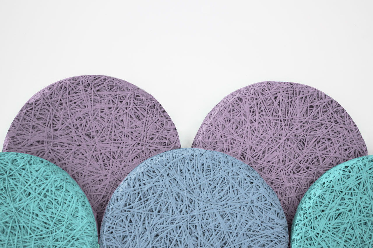 Five round, textured mats overlap each other. Three are purple and two are teal. The mats feature a crisscross, string-like pattern and are arranged against a plain white background.