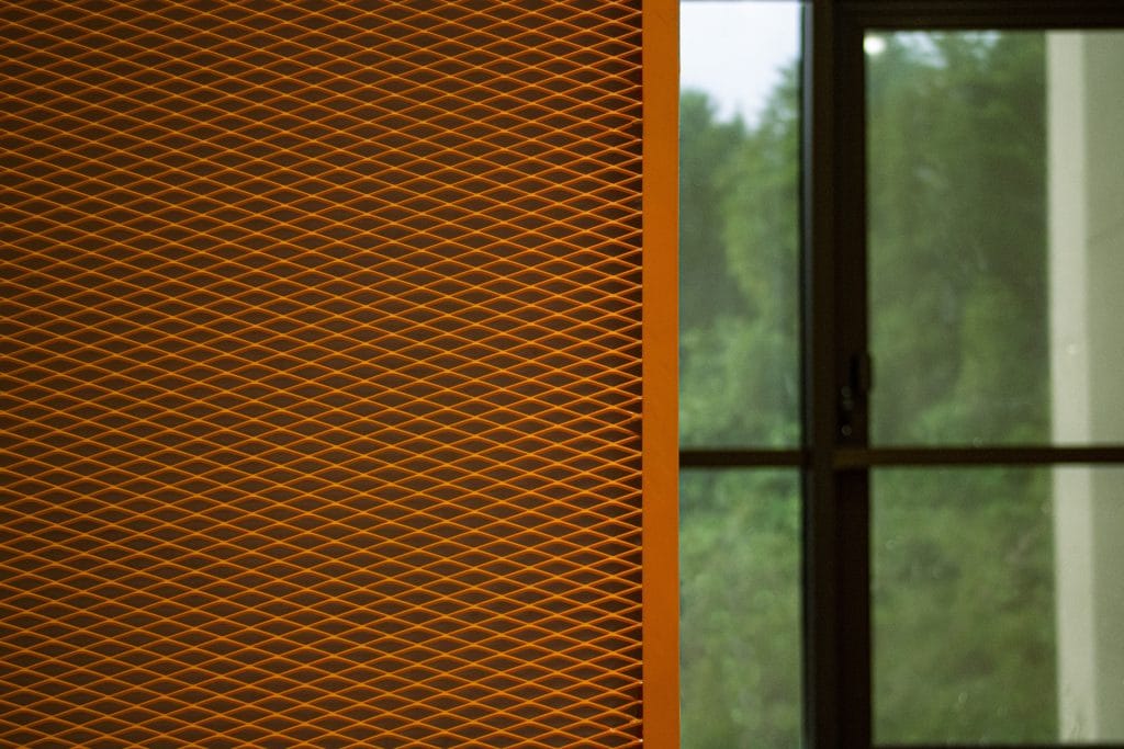 A close-up of an orange patterned wall panel on the left side, with a glass window and green trees visible outside on the right side of the image.