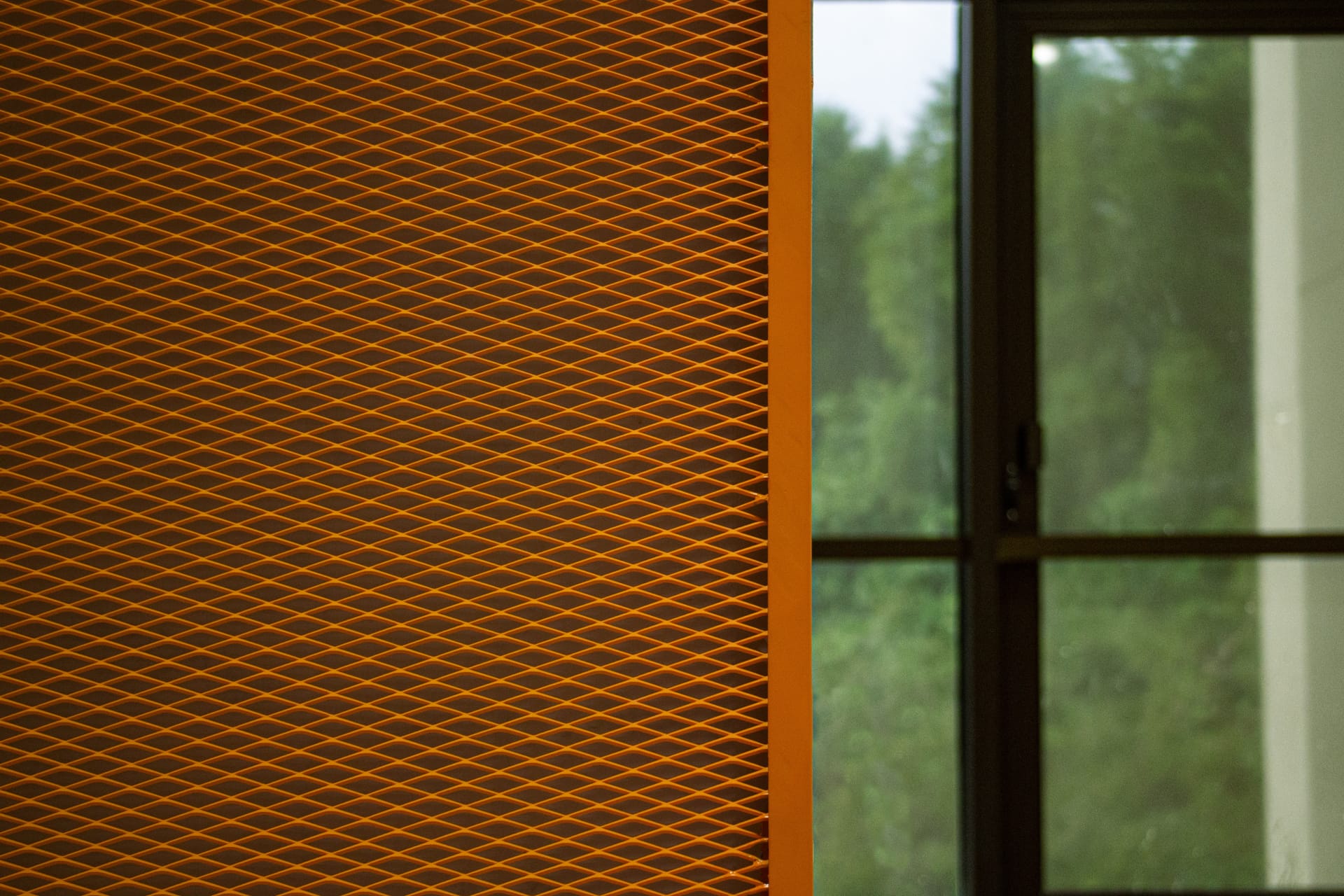 A close-up of an orange patterned wall panel on the left side, with a glass window and green trees visible outside on the right side of the image.