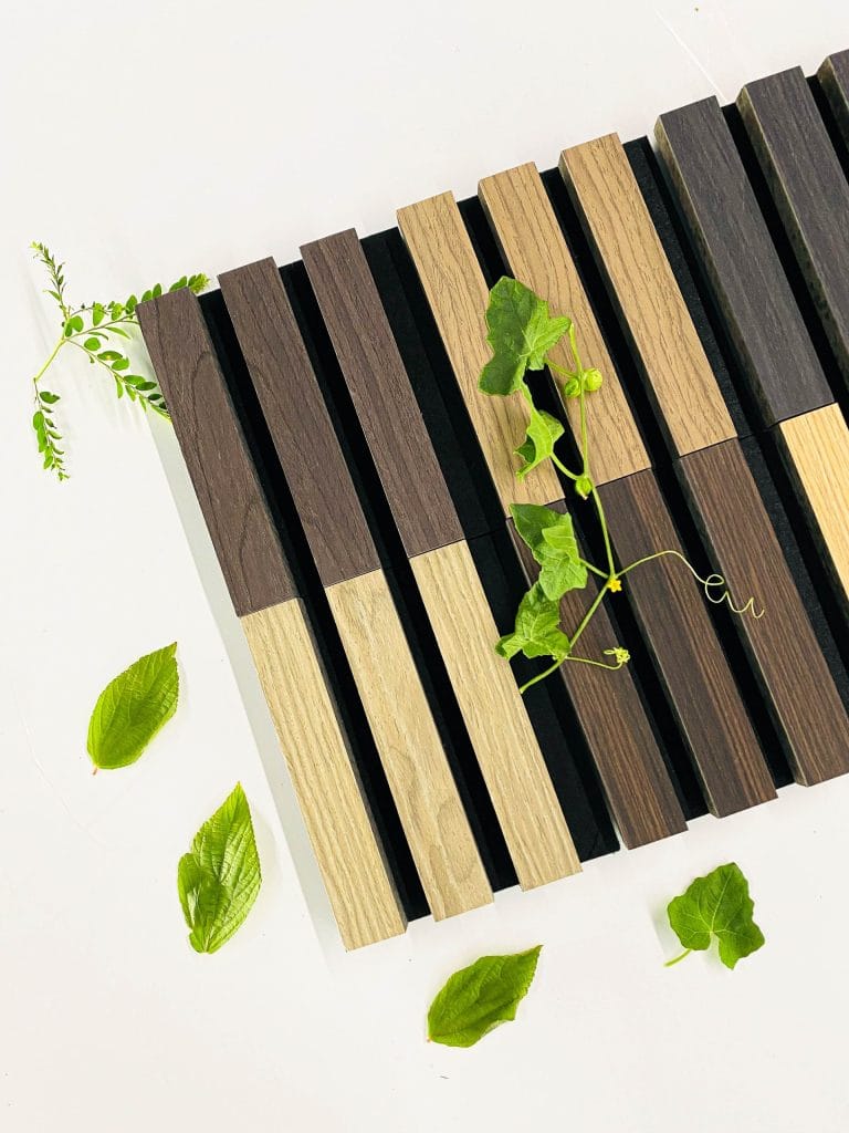 A pattern of alternating dark and light wooden slats arranged vertically, with green leaves and vines placed on and around the wood on a white surface.