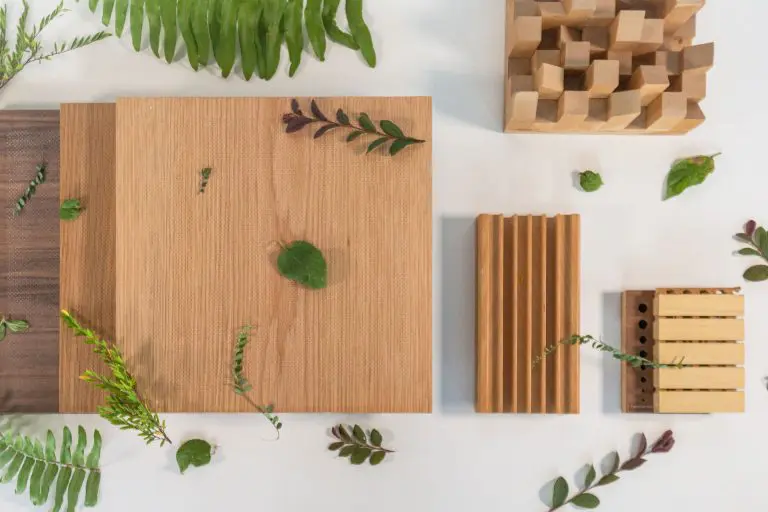 Wooden panels and blocks of different textures and sizes arranged on a white surface, surrounded by green leaves and ferns.