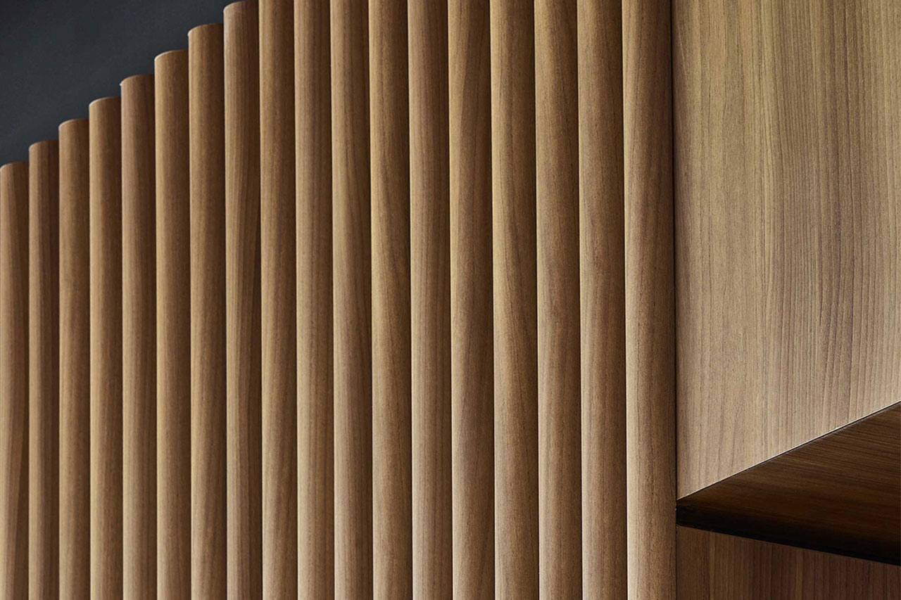 Close-up of a modern wooden wall with vertical slats, showing the natural grain of the wood and a sharp corner where the slats meet a smooth wooden surface.