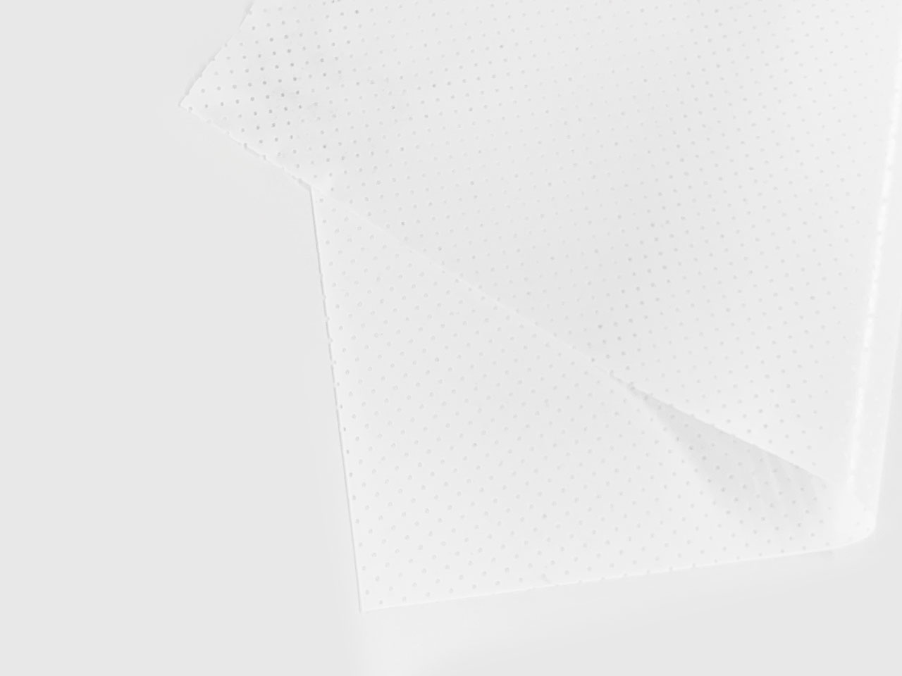 A close-up of two overlapping sheets of translucent, white, perforated material on a plain white surface. The small, evenly spaced holes give a dotted pattern to the sheets.