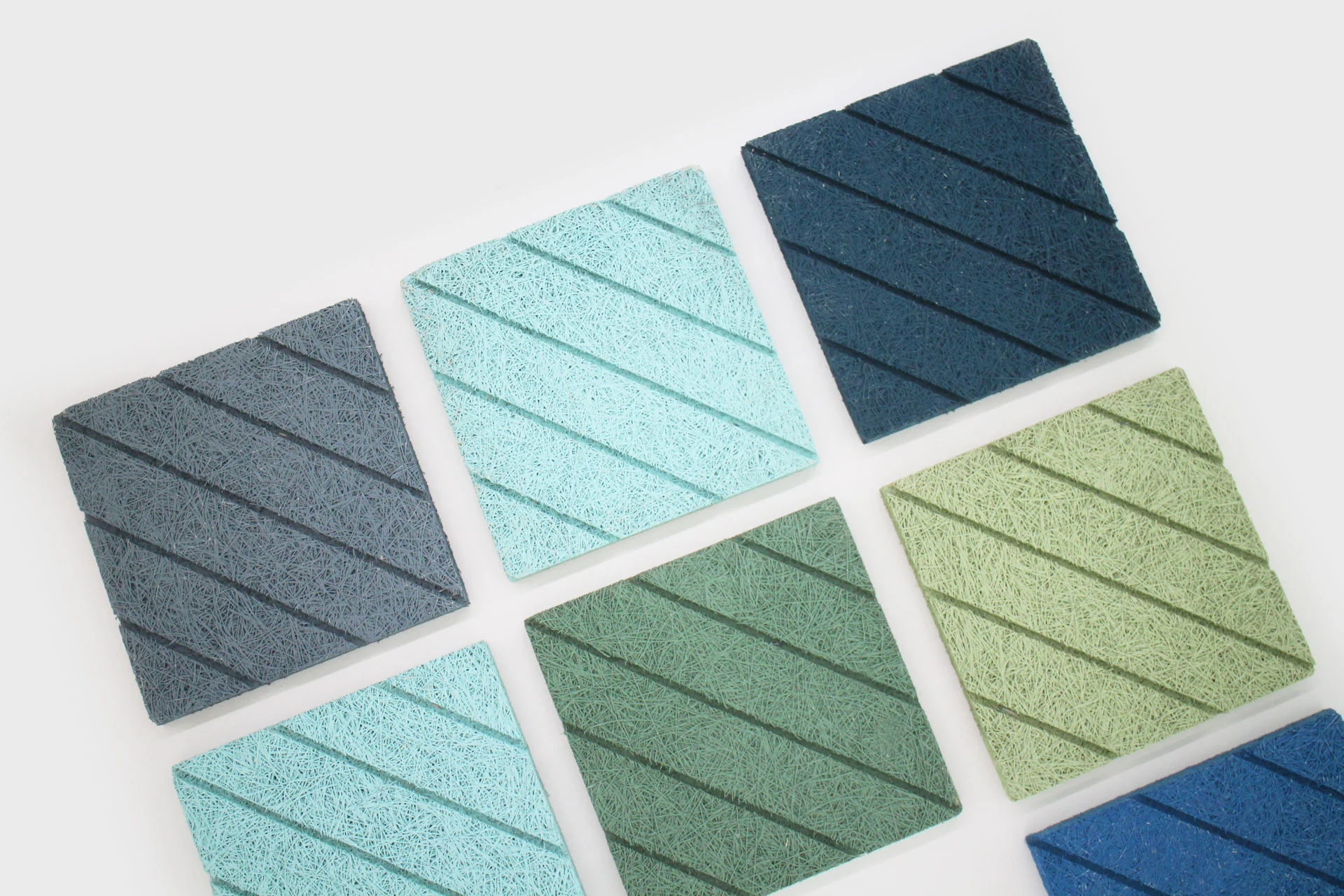 Eight square tiles in various shades of blue and green, each with a diagonal line pattern, are arranged on a white background in two rows.