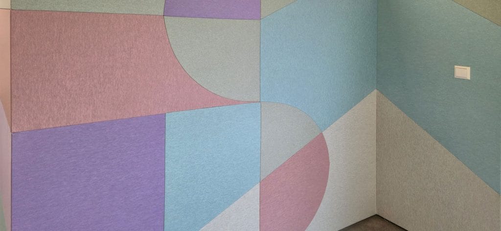 Geometric wall art with pastel-colored panels in shades of blue, purple, pink, and gray, forming intersecting shapes and lines. A white electrical switch is visible on the right side of the wall.