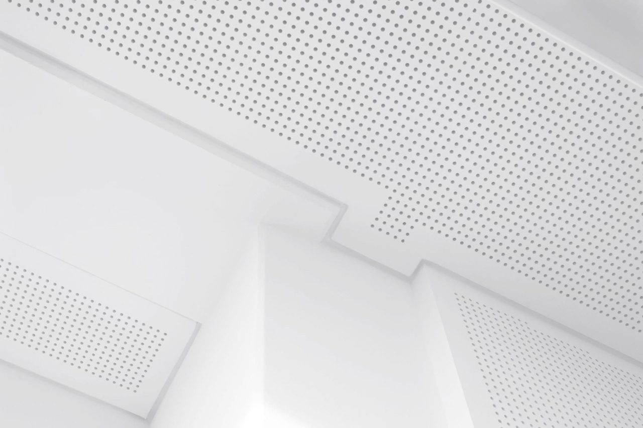 White perforated ceiling panels arranged geometrically, creating a modern, minimalist architectural look with clean lines and soft lighting.