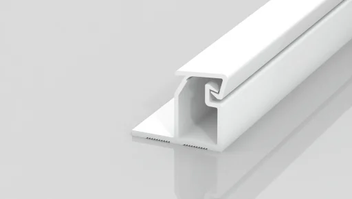 A white plastic or metal trim piece with a grooved, angular profile, lying on a light grey reflective surface. The design features an overhanging lip and an open channel along its length.