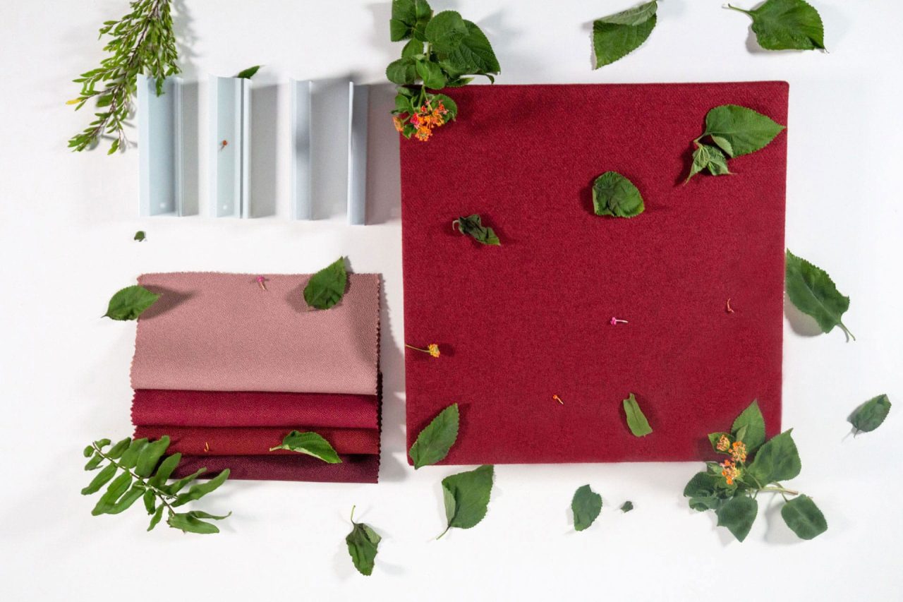 A flat lay of burgundy and pink fabric swatches, paint samples in neutral tones, and scattered green leaves and small flowers on a white background.