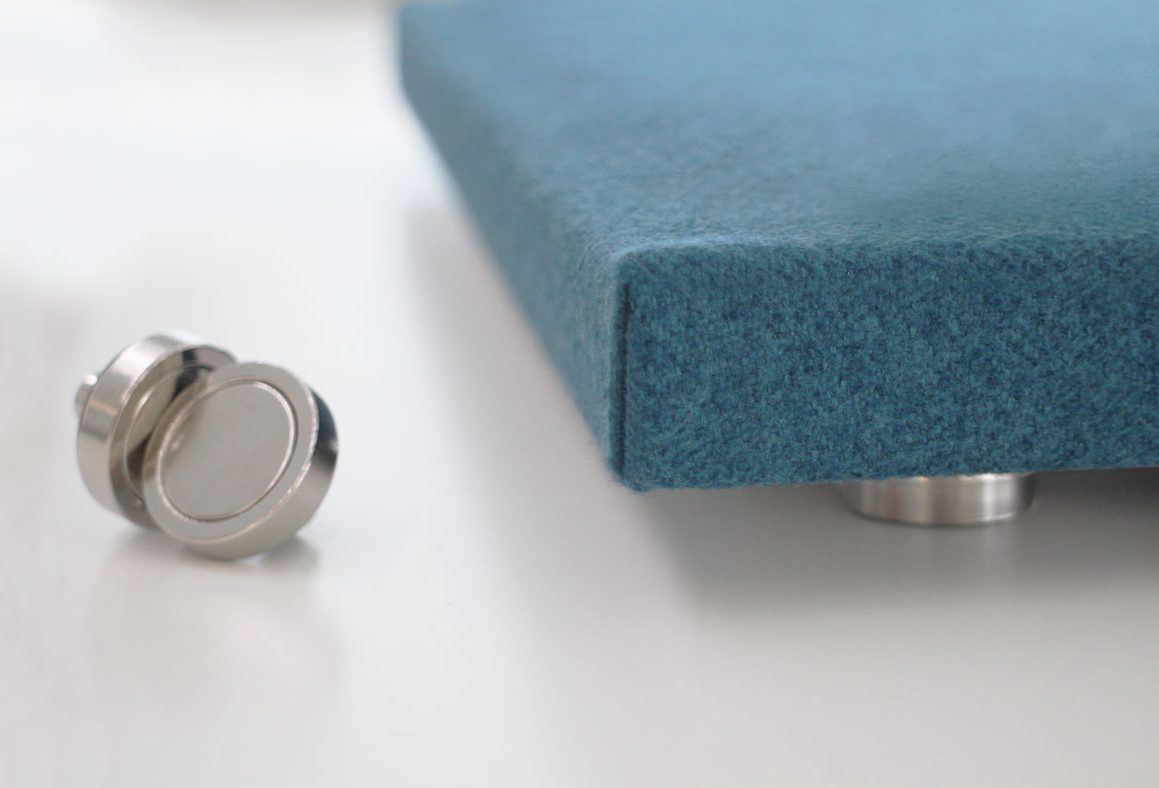 A close-up of a blue, fabric-covered object on metal feet, with a small, round silver knob or fastener placed nearby on a white surface.