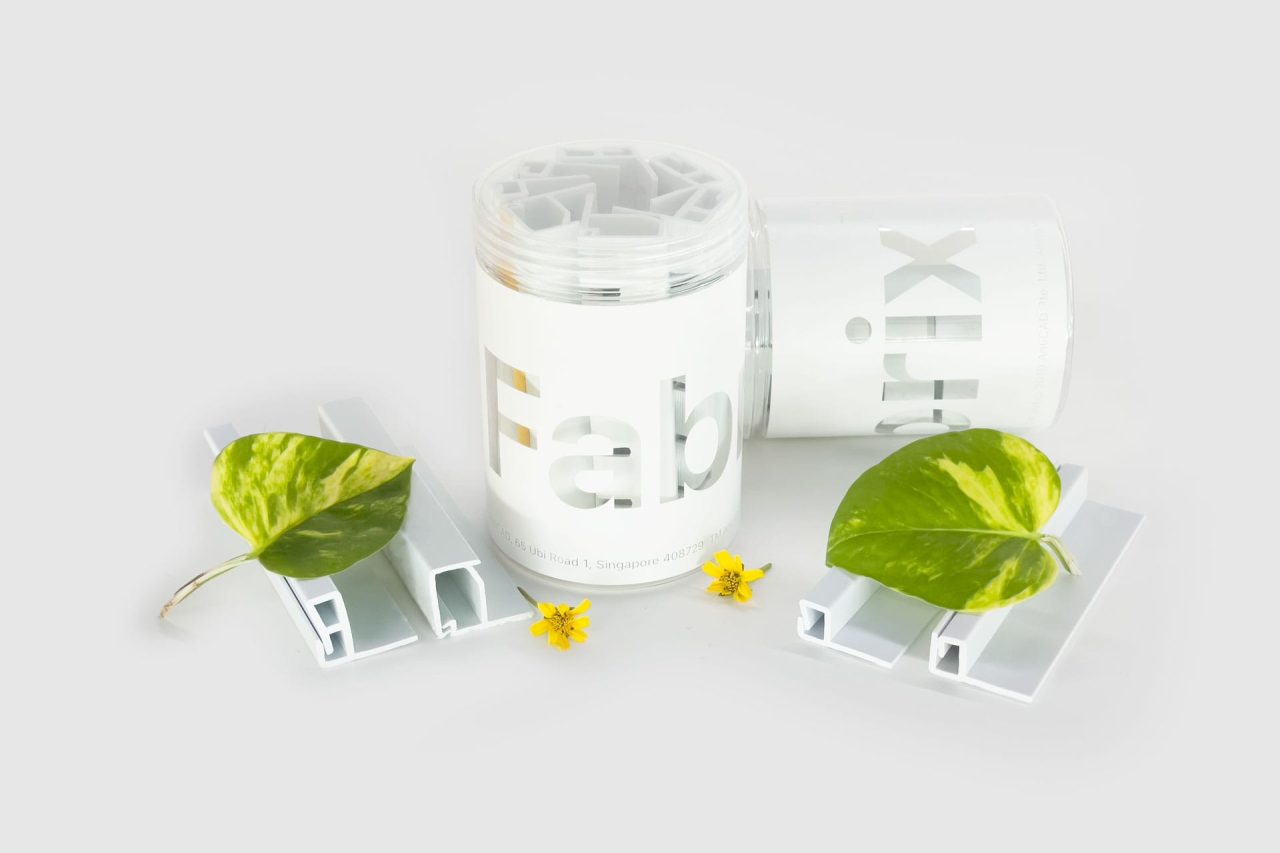 Two white containers labeled Fab and rt ix with white plastic pieces, green leaves, and small yellow flowers arranged on a light gray background.