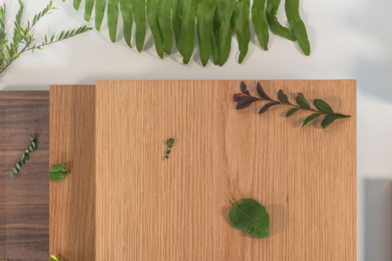 A wooden surface with scattered green leaves and sprigs, with a fern partially visible at the top on a white background.