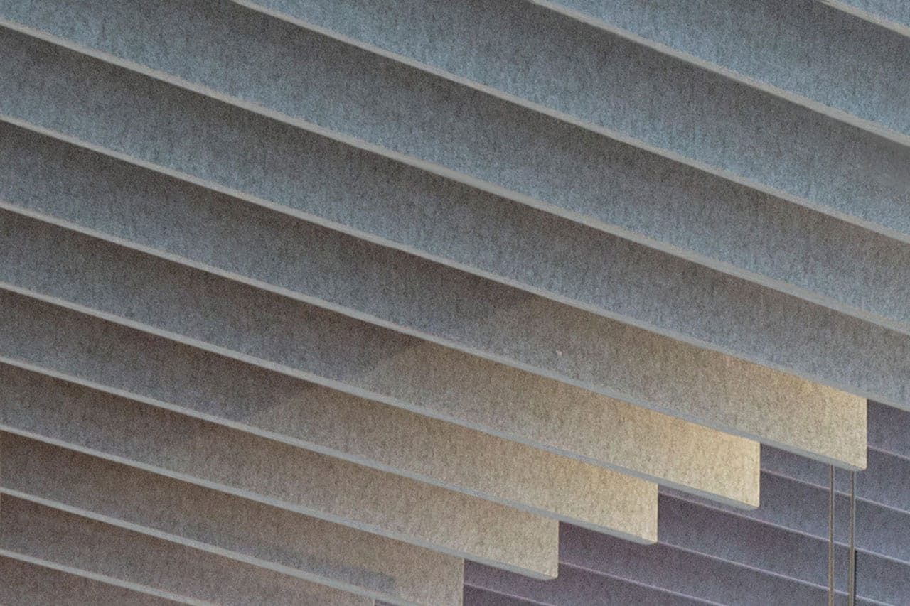 Close-up of a series of gray, angled horizontal slats or panels, creating a repetitive geometric pattern with varying shades due to lighting and shadows.