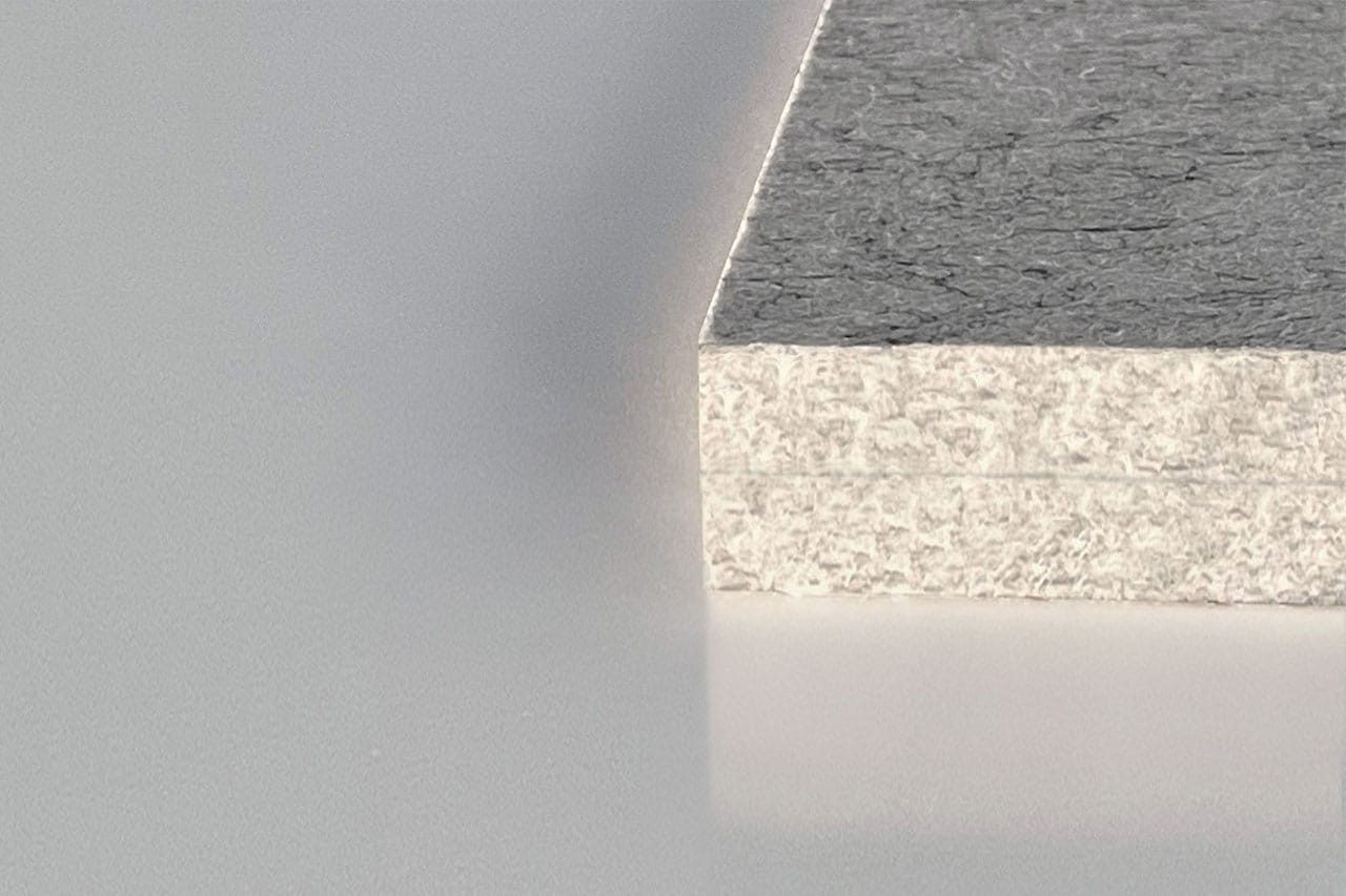 Close-up of the edge of a gray composite board, showing its layered, textured structure against a smooth, light-colored background.