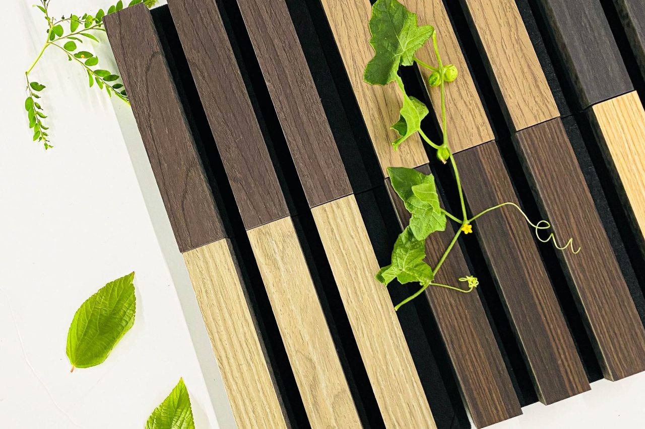 A pattern of alternating dark and light wooden slats arranged vertically, with green leaves and vines placed on and around the wood on a white surface.