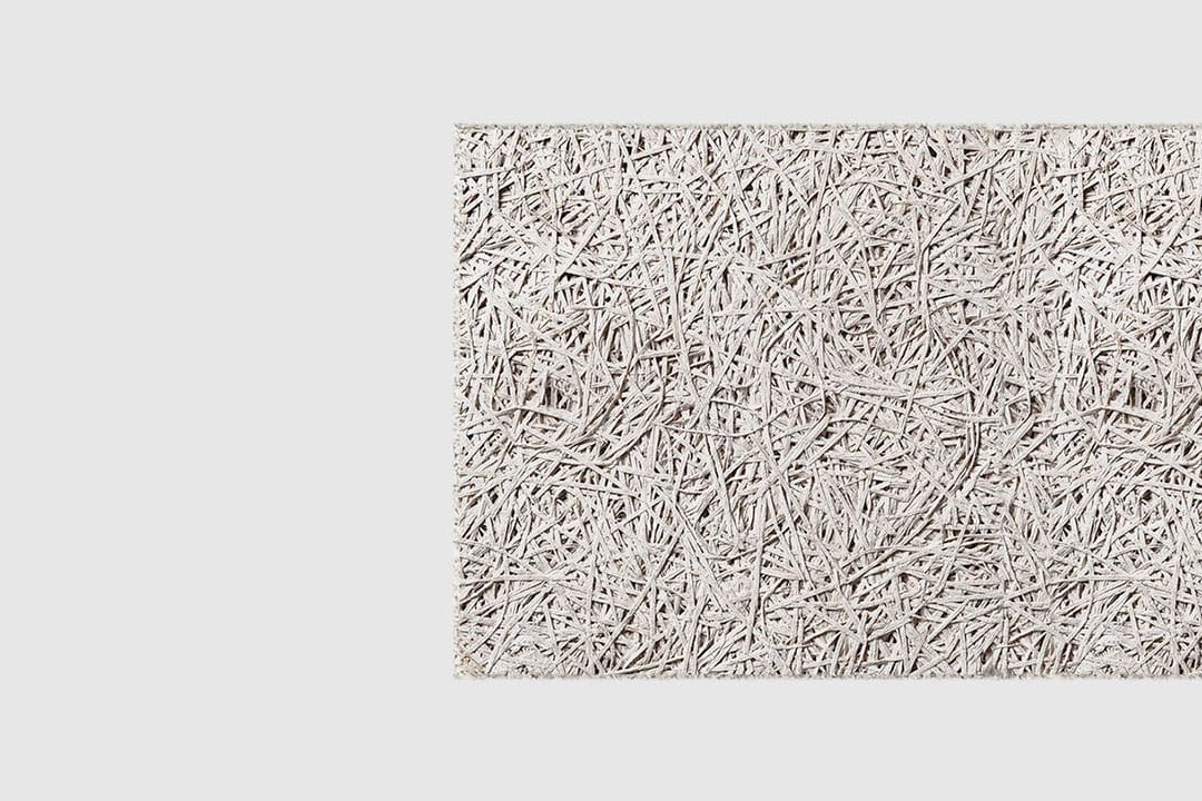 A close-up view of a textured, light grey rectangular panel made of compressed wood fibers on a plain white background.