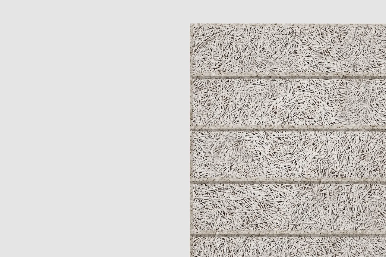 Close-up view of a light gray textured wall panel made of compressed wood wool fibers, divided by horizontal grooves into four sections, with a plain light gray background on the left.
