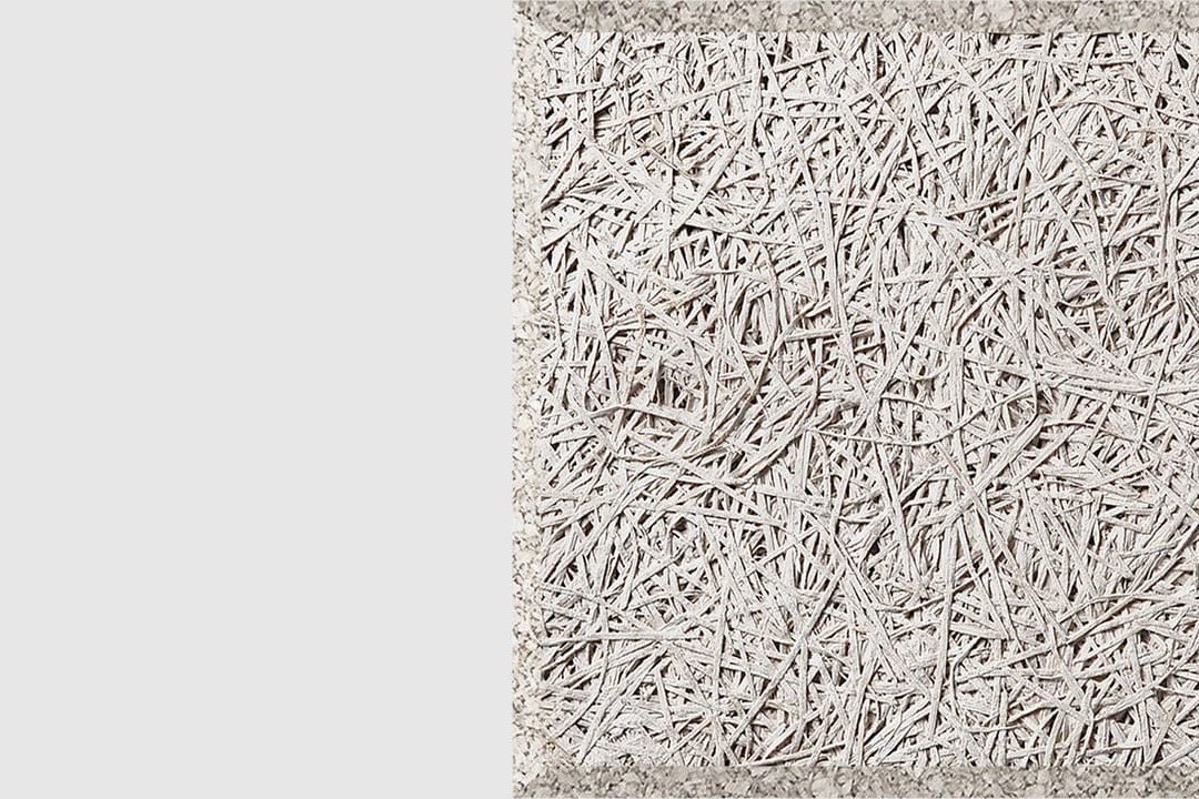 A close-up of a textured, light gray panel made of compressed wood fibers, arranged in a random, crisscross pattern, with a rough, fibrous surface and defined rectangular edges.